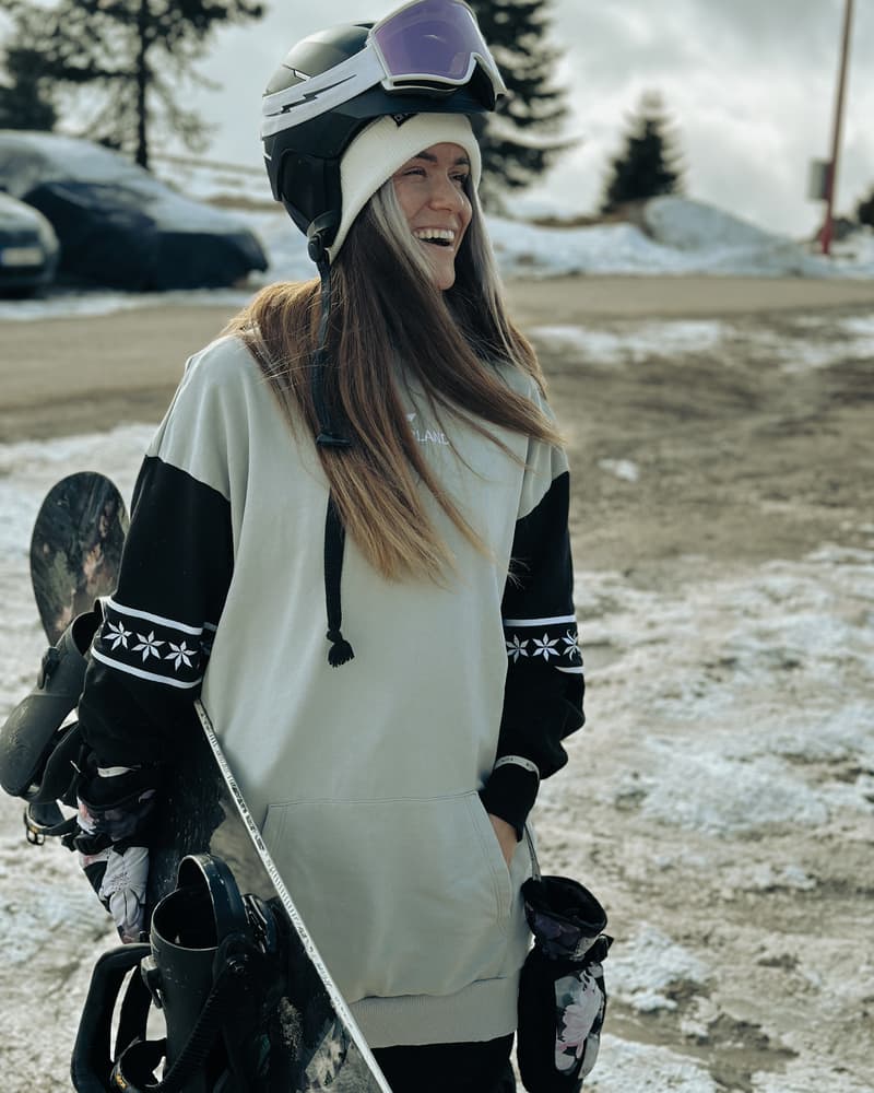 Žena u beloj varijanti Wonderland duksa LONG sa skijaškom opremom na snegu